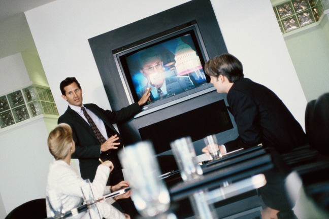 A group of people in suits and ties around a tv.